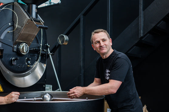 Owner Andrew Smart leaning on a large black coffee roasting machine 