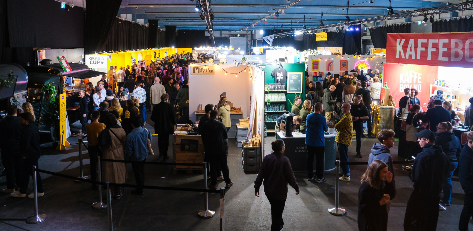 The show floor, busy with attendees, with Roaster's Village as a bright yellow and equipment booths on the right